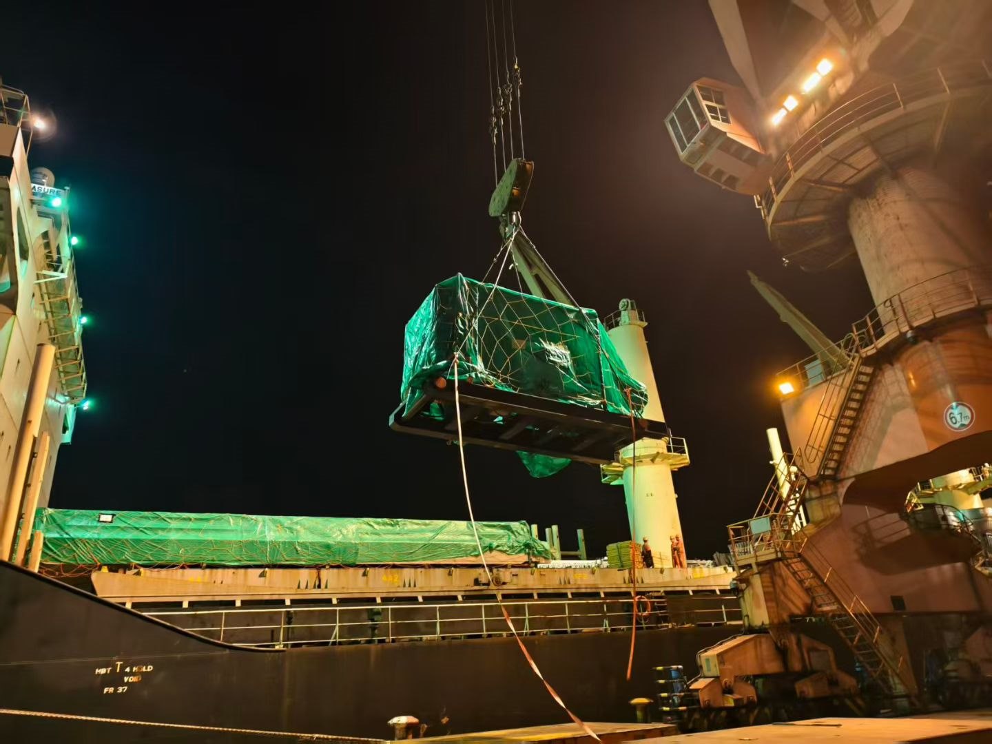 Packaged breakbulk cargo being lifted onto a vessel at night